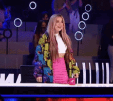 a woman wearing a colorful jacket and a pink skirt is standing in front of a microphone