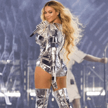 a woman in a silver bodysuit and boots is singing into a microphone