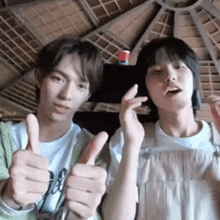 two young men are giving each other thumbs up .