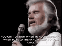 a man with a beard is singing into a microphone with a quote on it .
