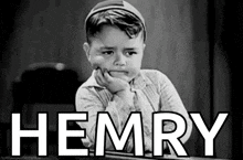 a little boy is sitting at a desk with his hand on his chin and the word hemry written on the screen .