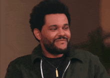 a man with a beard wearing a green jacket and a necklace is smiling .