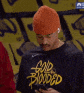 a man wearing an orange hat and a black shirt that says gold blooded