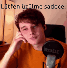 a young man sitting in front of a rode microphone talking on a cell phone