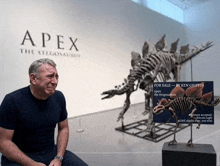 a man sits in front of a display of a stegosaurus