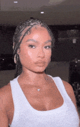 a woman with braids is wearing a white tank top and a necklace