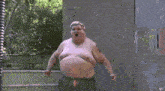 a shirtless fat man with a tattoo on his arm is standing in front of a fence
