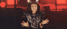 a woman is standing on a stage with her hands in the air and a crown on her head .