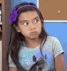 a little girl wearing a purple headband and a t-shirt with a wolf on it is making a face .