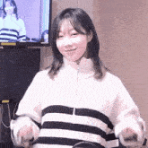a woman wearing a black and white striped sweater is standing in front of a television