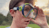 a young man wearing a blue and green diving mask covering his eyes with his hand