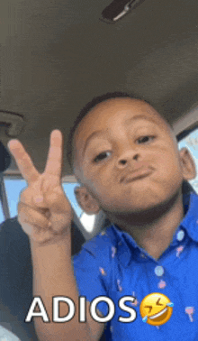 a young boy in a blue shirt is giving a peace sign with the word adios written below him