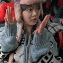 a young girl wearing a hat and a sweater is making a peace sign .