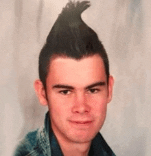a young man with a mohawk hairstyle is looking at the camera .