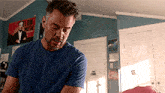 a man in a blue shirt is standing in a room with a poster on the wall that says ' lon musk '