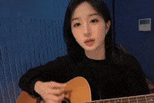 a girl is playing an acoustic guitar in front of a blue wall