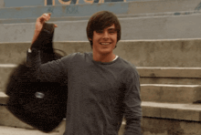 a man in a grey shirt is holding a black bag that says ' herschel supply co ' on it