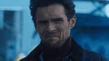 a man with a beard and a black jacket looks at the camera