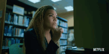 a woman sitting in front of a computer with a netflix logo on the bottom
