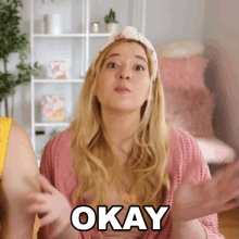 a woman in a pink cardigan says okay with her hands outstretched