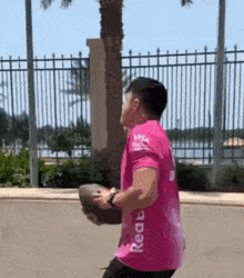 a man in a pink shirt is holding a rugby ball .
