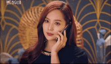 a woman with red hair is talking on a cell phone in front of a wall .