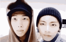 two young men wearing hats and hoodies are looking at the camera .