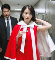 a woman in a red dress and white cape stands next to a man in a suit and tie