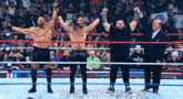 a group of men are standing in a wrestling ring with their arms up