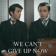 two men sitting next to each other with the words we can 't give up now behind them