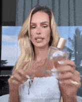a woman in a white top holds a bottle of perfume in her hands