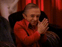 a man in a red shirt is clapping his hands in front of a red curtain