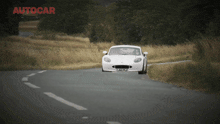 a white sports car is driving down a road with autocar written on the bottom right