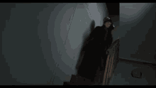 a man in a black coat is walking down stairs in a dark room .