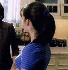 a woman in a blue striped shirt stands in a kitchen