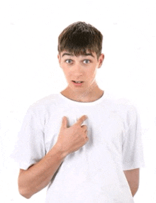 a young man in a white t-shirt is pointing at his chest with his hand .