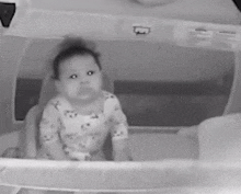 a black and white photo of a baby sitting in a crib