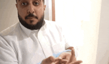 a man with a beard is wearing a white shirt and blue gloves and is holding something in his hands .