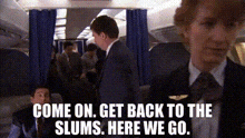 a man in a suit and tie is standing in a crowded airplane .