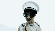 a woman wearing a hat and sunglasses holds her hands up in the air