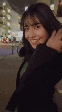 a woman in a black jacket is smiling with her hand in her hair