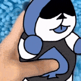 a person is holding a blue and white cartoon character with their tongue out .