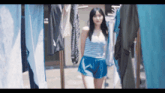 a woman in blue shorts is walking through a row of clothes