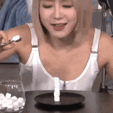 a woman is sitting at a table holding a spoon and a plate of sugar cubes .