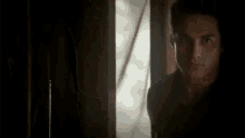 a man is standing in a dark room in front of a window .