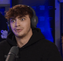 a man wearing headphones and a black hoodie is talking into a microphone