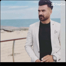 a man with a beard is leaning against a wall and smoking a cigarette in front of the ocean