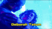 a man is holding a woman in a blue light with the name deborah tatum above them