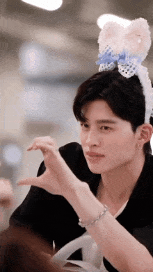 a young man wearing a headband with bunny ears is making a heart shape with his hands .