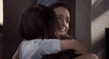 two women are hugging each other in a living room .